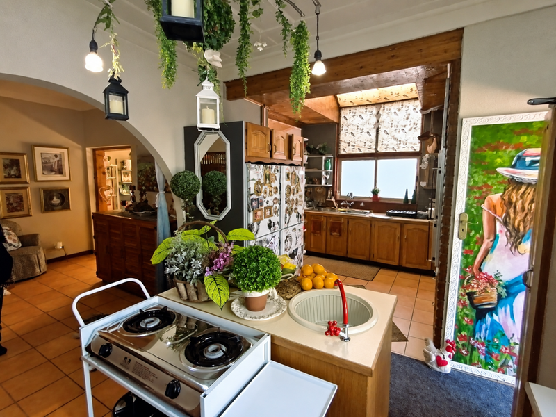 A rustic kitchen featuring wooden cabinetry, tiled flooring, and exposed ceiling beams, with an open-plan layout connecting to the adjacent living area.