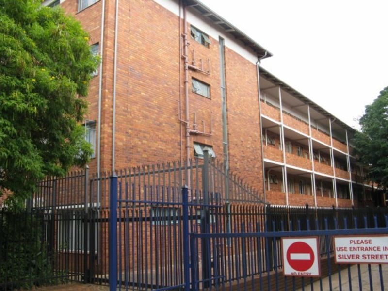 Exterior view of a multi-story brick apartment building featuring security fencing and external access balconies.