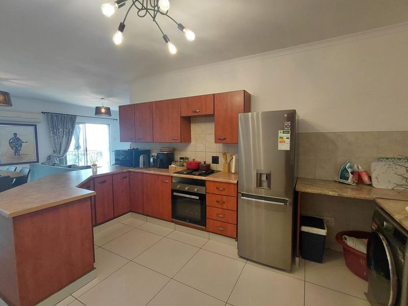 Open plan kitchen featuring wooden cabinetry, laminate countertops, built-in oven and hob, tiled flooring, and a breakfast bar area.
