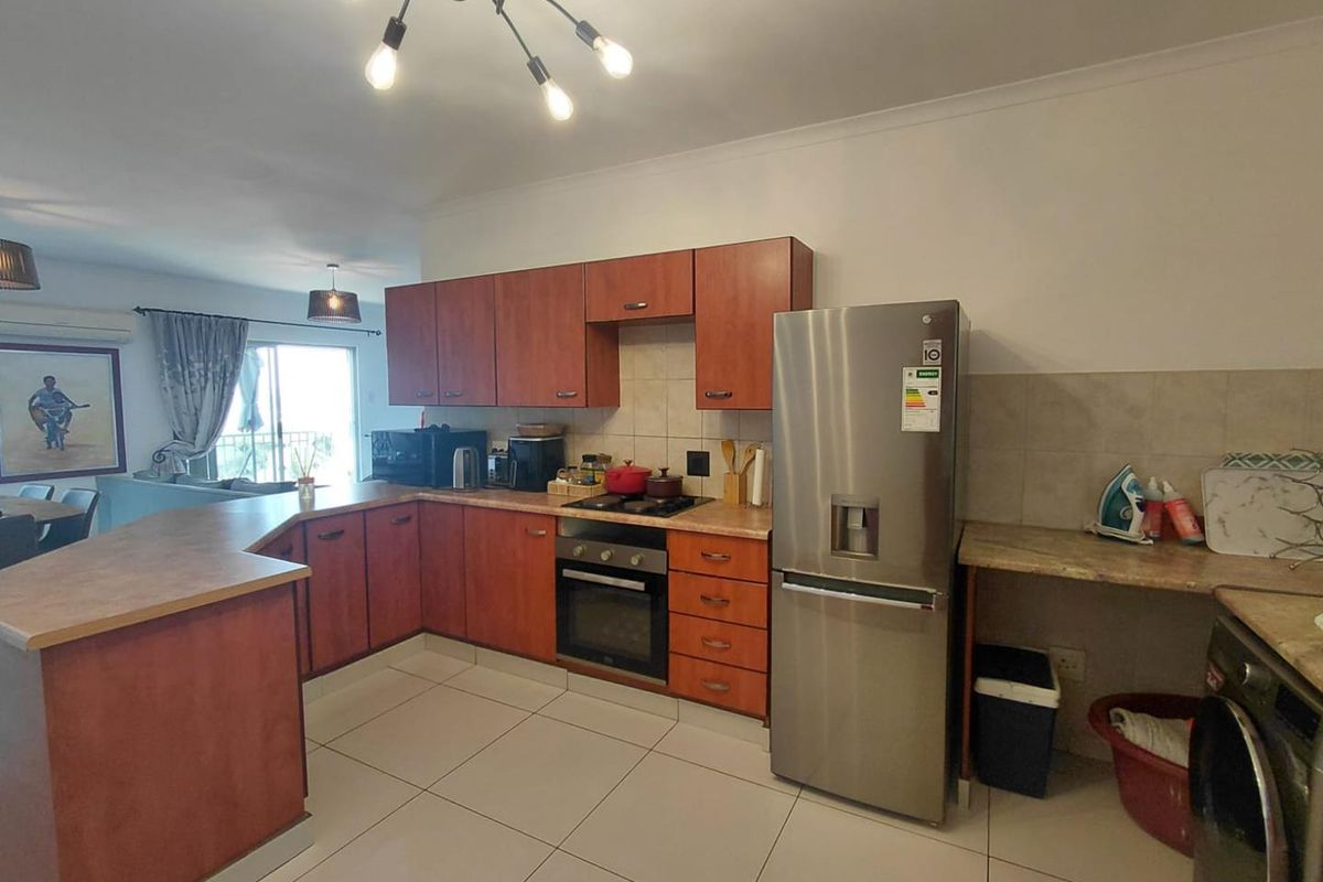 Open plan kitchen featuring wooden cabinetry, laminate countertops, built-in oven and hob, tiled flooring, and a breakfast bar area.