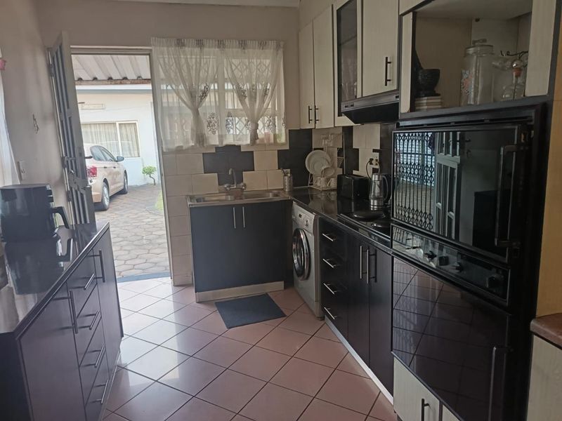 A functional kitchen featuring dark cabinetry, integrated oven, extractor fan, and tiled flooring with direct access to the exterior driveway area.