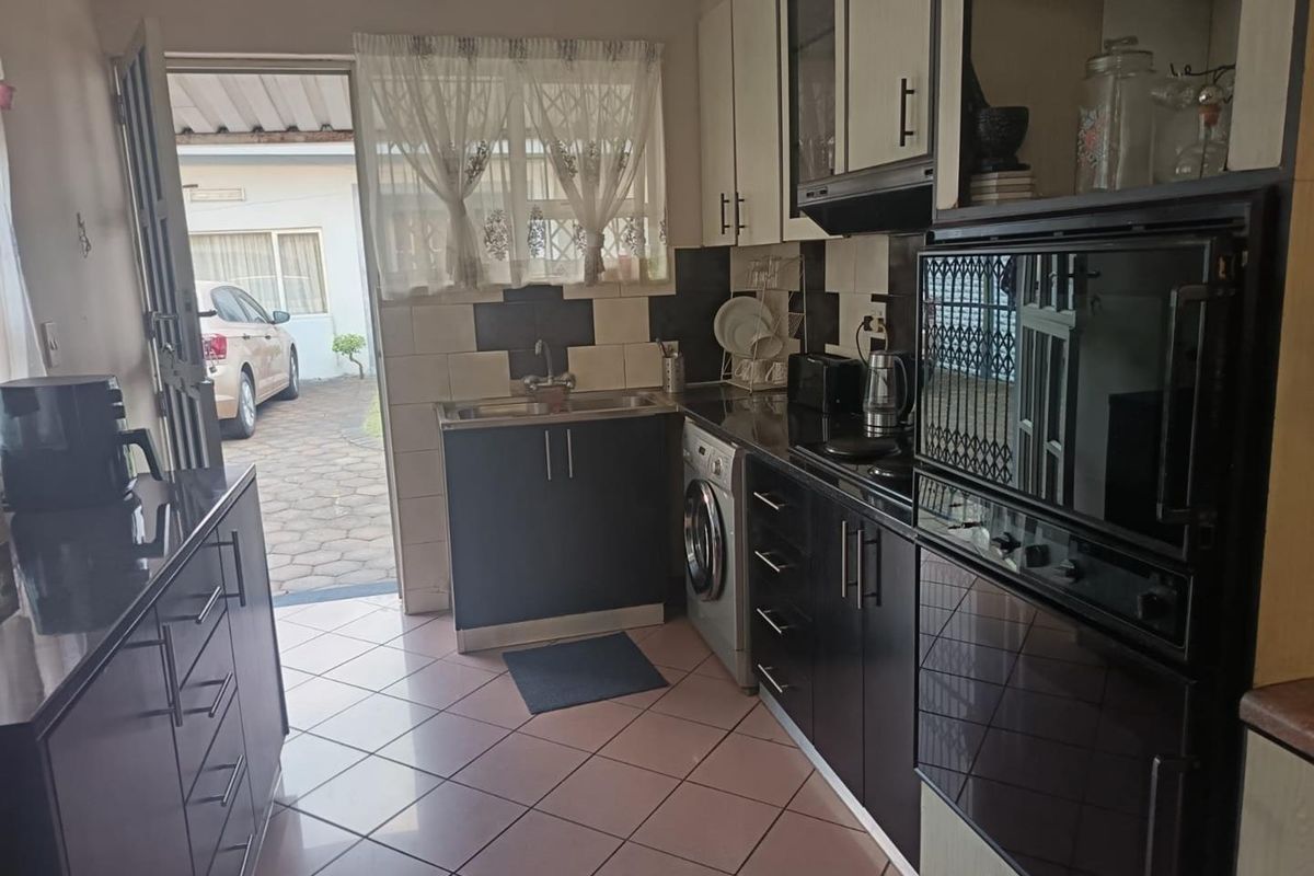 A functional kitchen featuring dark cabinetry, integrated oven, extractor fan, and tiled flooring with direct access to the exterior driveway area.