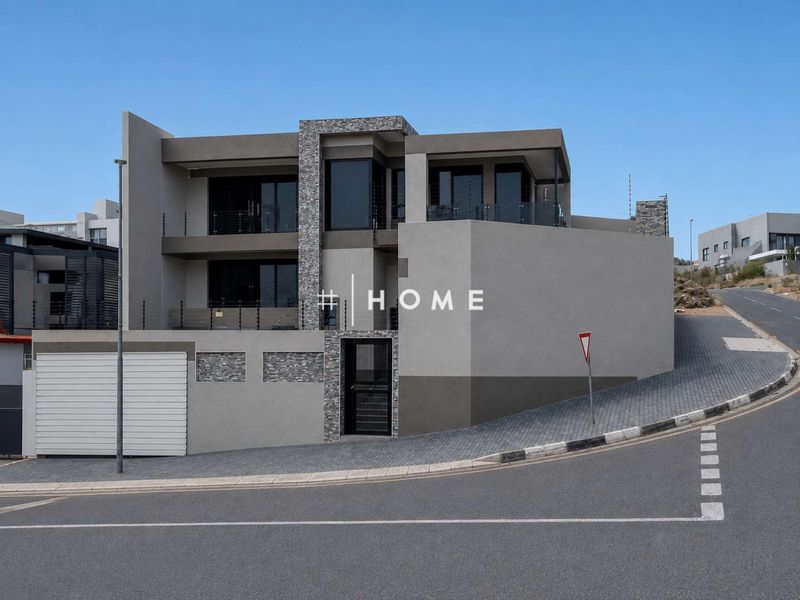 Modern double-story residential property featuring contemporary stone cladding, glass balcony balustrades, and secure perimeter fencing with a paved driveway.
