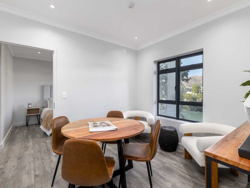 A bright and modern living area featuring neutral walls, laminate flooring, recessed downlights, and a large black-framed window with views.