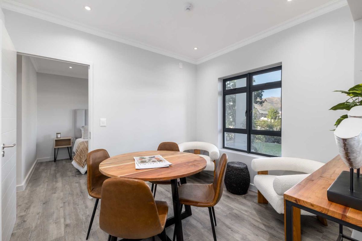 A bright and modern living area featuring neutral walls, laminate flooring, recessed downlights, and a large black-framed window with views.
