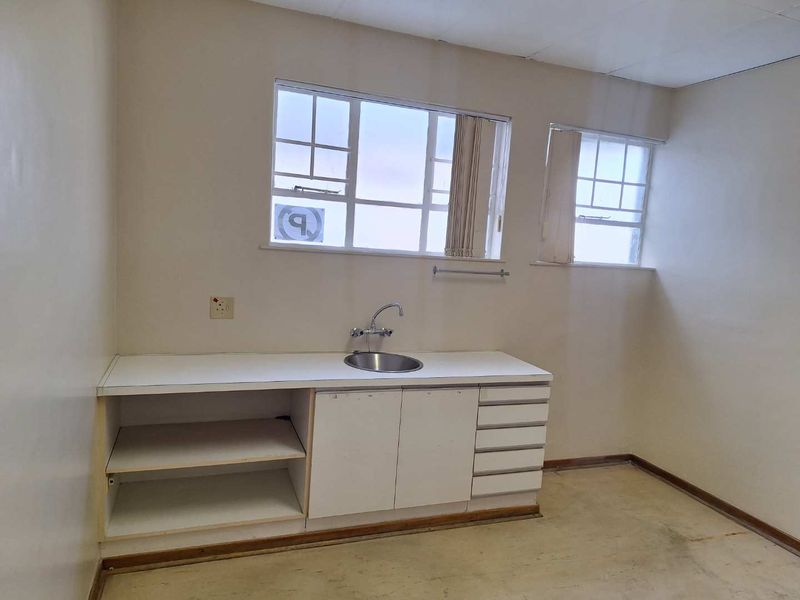 A functional kitchenette area featuring built-in cabinetry, a stainless steel sink, and natural light from multi-pane windows, ready for renovation or modernization.