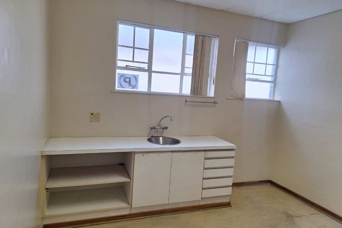 A functional kitchenette area featuring built-in cabinetry, a stainless steel sink, and natural light from multi-pane windows, ready for renovation or modernization.