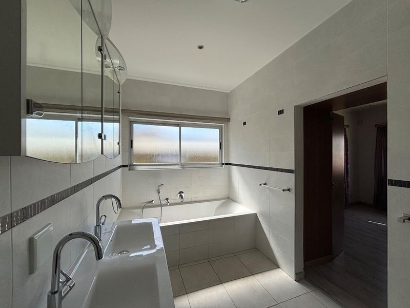 A clean, modern bathroom featuring a built-in bathtub, double vanity with chrome fixtures, and tiled finishes throughout.