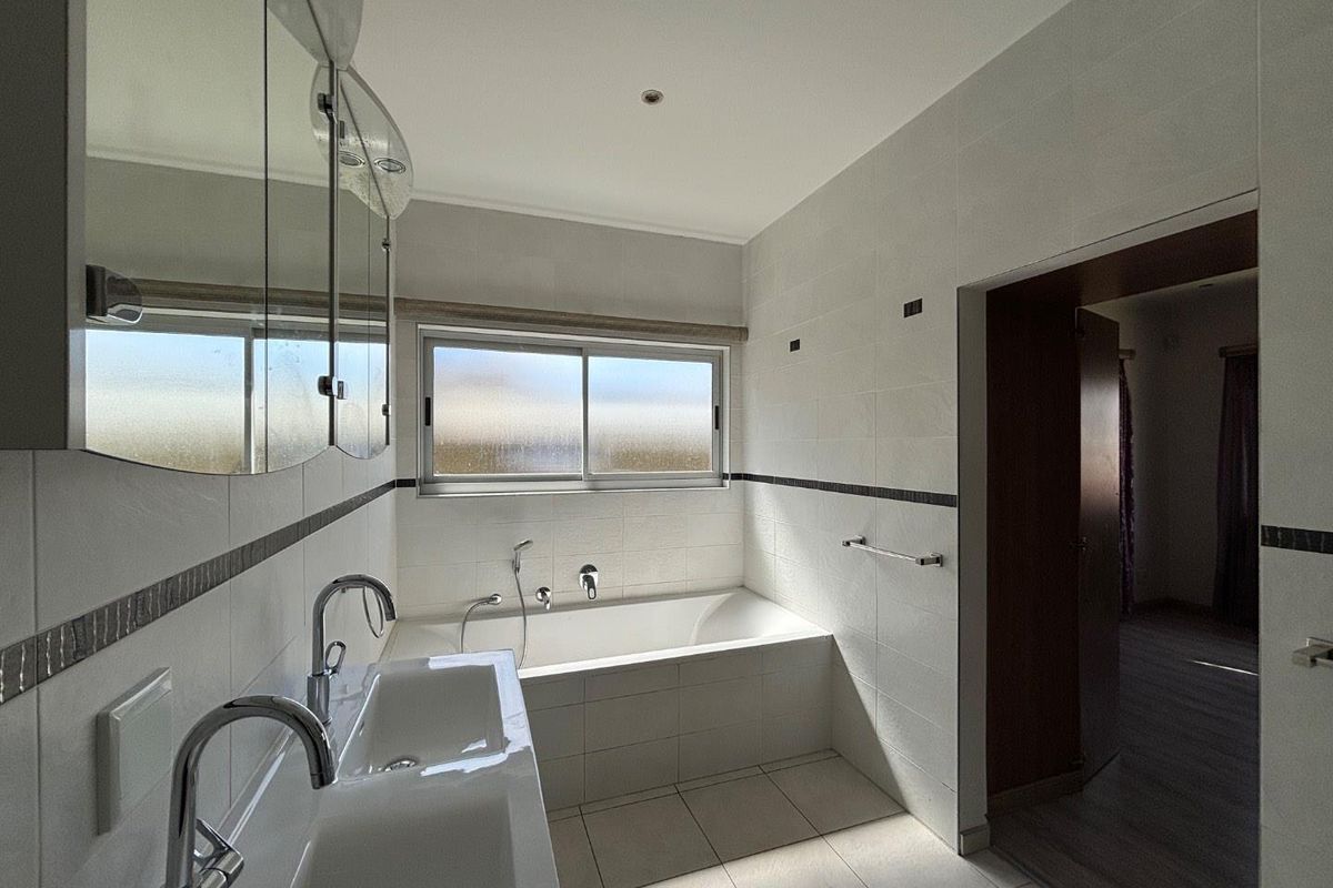 A clean, modern bathroom featuring a built-in bathtub, double vanity with chrome fixtures, and tiled finishes throughout.