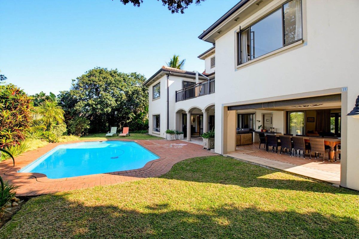 Rear view of the property featuring a swimming pool, brick paved patio area, covered outdoor entertainment space, and a well-maintained garden.