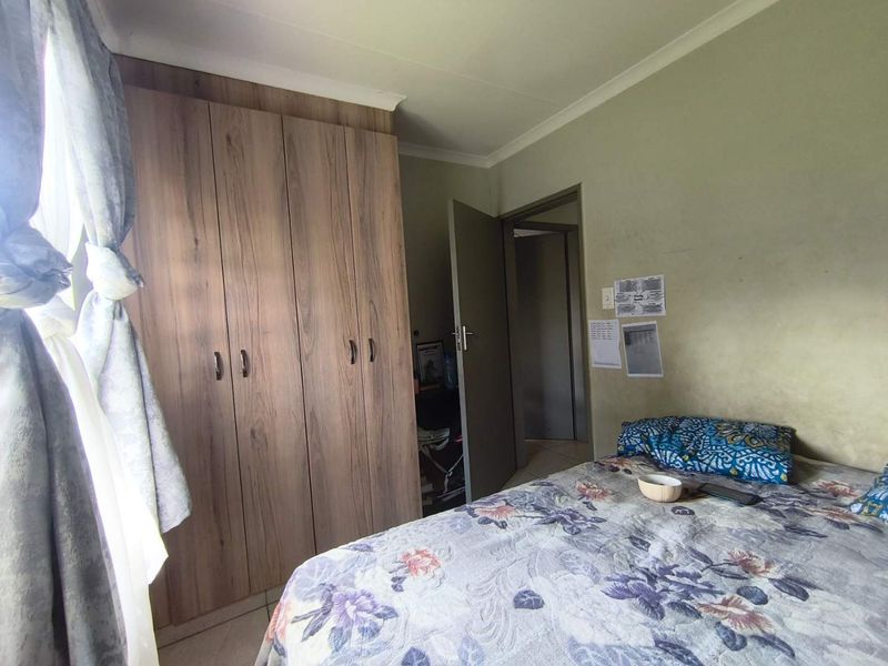 A functional bedroom featuring built-in wooden wardrobes, tiled flooring, and coved ceilings, providing a practical living space.