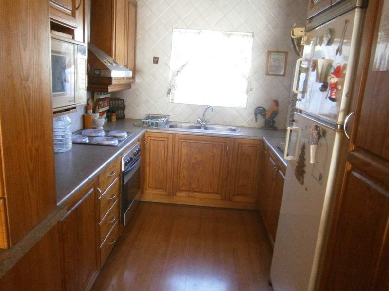 A functional kitchen featuring wooden cabinetry, laminate countertops, a double basin sink, and built-in appliances including an oven and hob.
