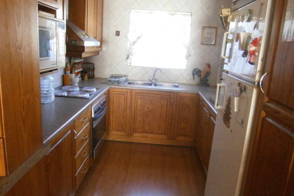 A functional kitchen featuring wooden cabinetry, laminate countertops, a double basin sink, and built-in appliances including an oven and hob.