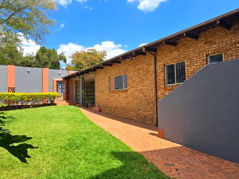 A well-maintained rear exterior view featuring an exposed brick facade, paved walkway, and a neatly landscaped garden area.
