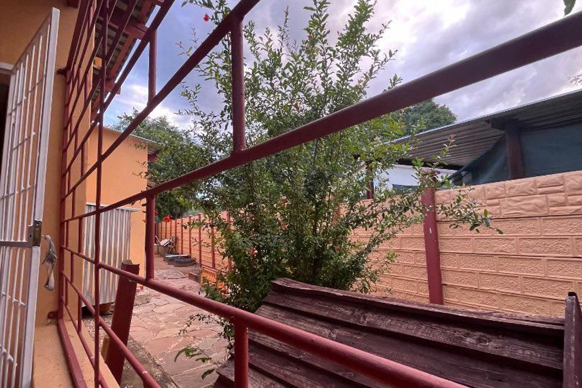 View of the rear exterior area featuring a paved walkway, perimeter precast walling, and security bars on the building structure.