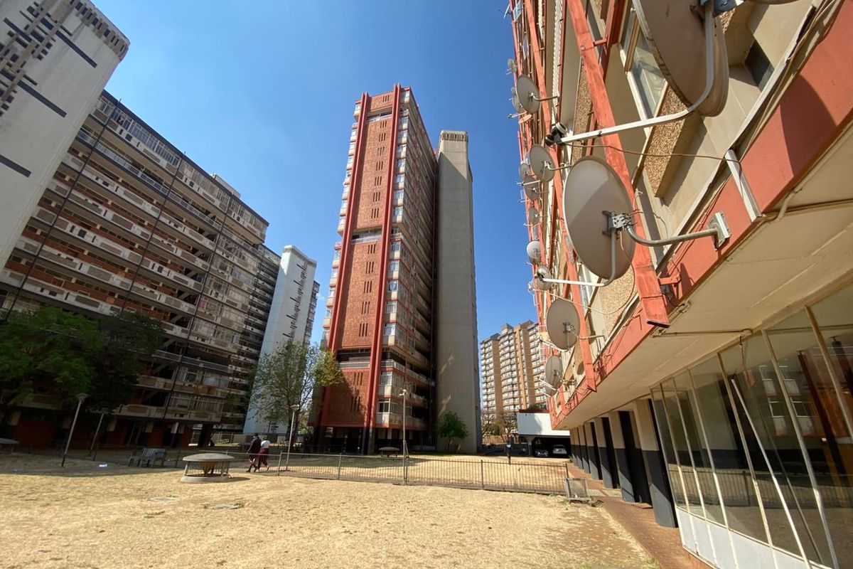 Exterior view of a high-rise apartment complex featuring brick facades, multiple satellite dish installations, and a shared open courtyard area.