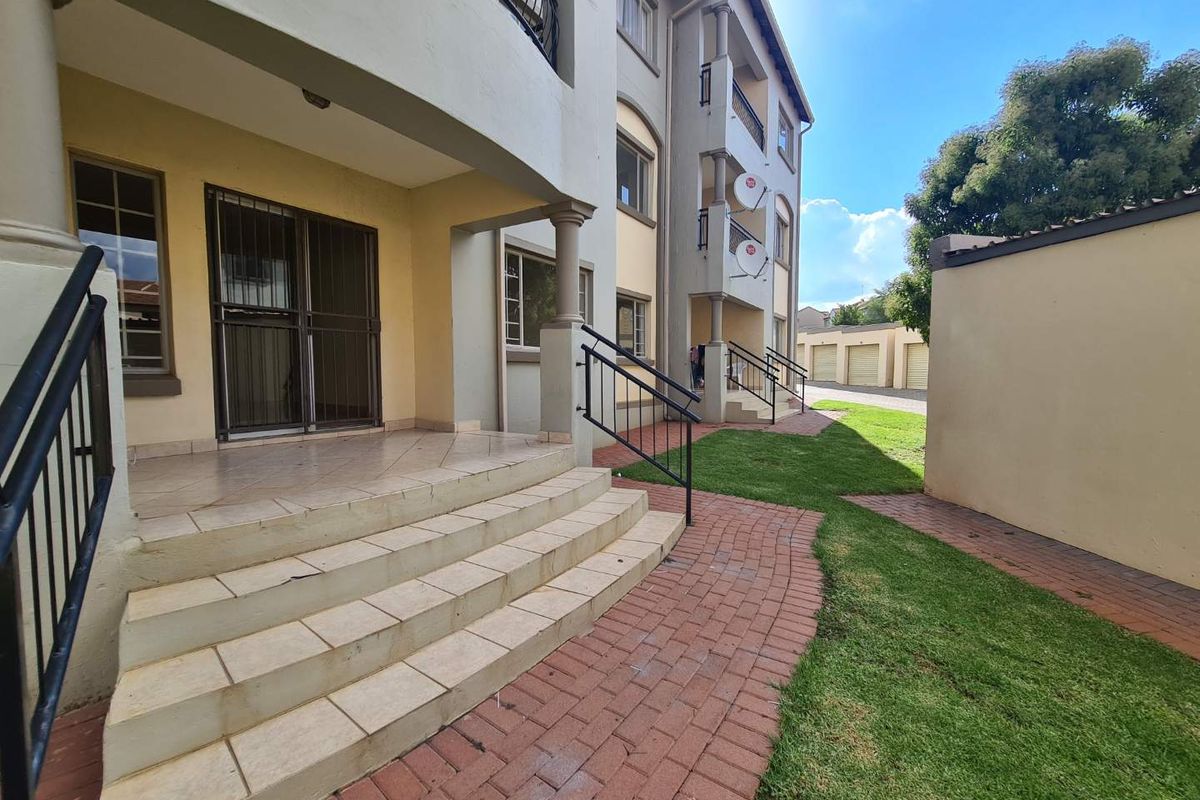 A view of the apartment building's rear exterior, featuring a tiled patio, paved walkways, and a well-maintained lawn area.