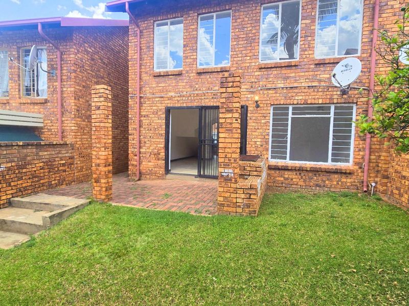 Rear view of a face brick townhouse featuring a paved patio area, built-in brick braai, and a private lawn.
