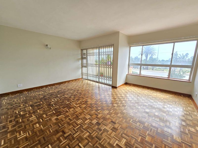 Spacious, empty living area featuring classic parquet flooring, large windows for natural light, and a secure sliding gate leading to the exterior.