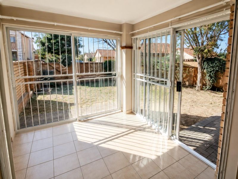 A bright, enclosed patio area featuring tiled flooring and large sliding glass doors with security gates, offering direct access to the rear garden.