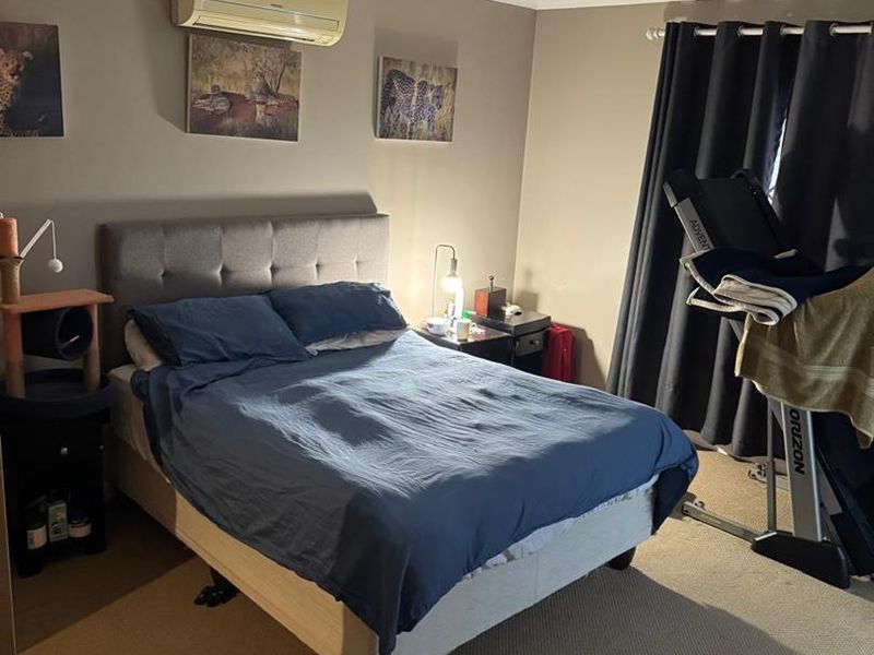 A functional bedroom featuring neutral wall tones, carpeted flooring, and a wall-mounted split-system air conditioning unit.