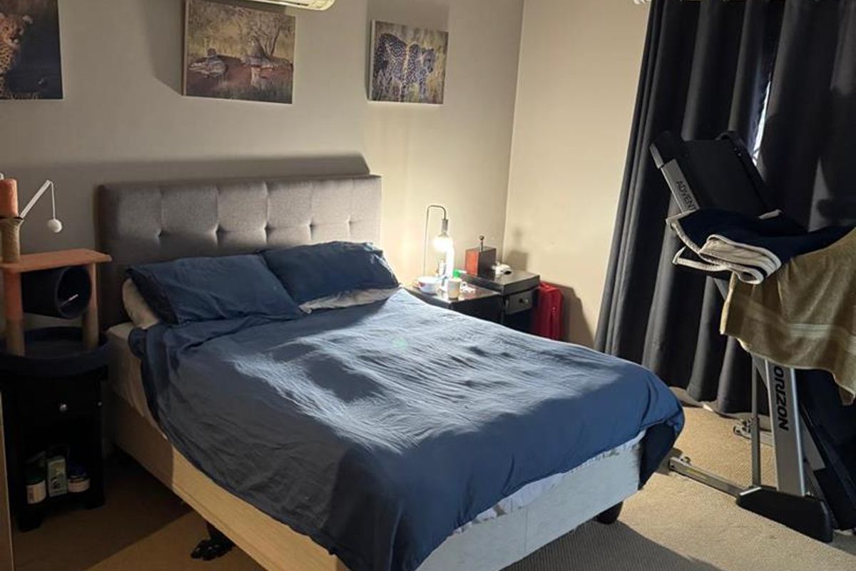 A functional bedroom featuring neutral wall tones, carpeted flooring, and a wall-mounted split-system air conditioning unit.
