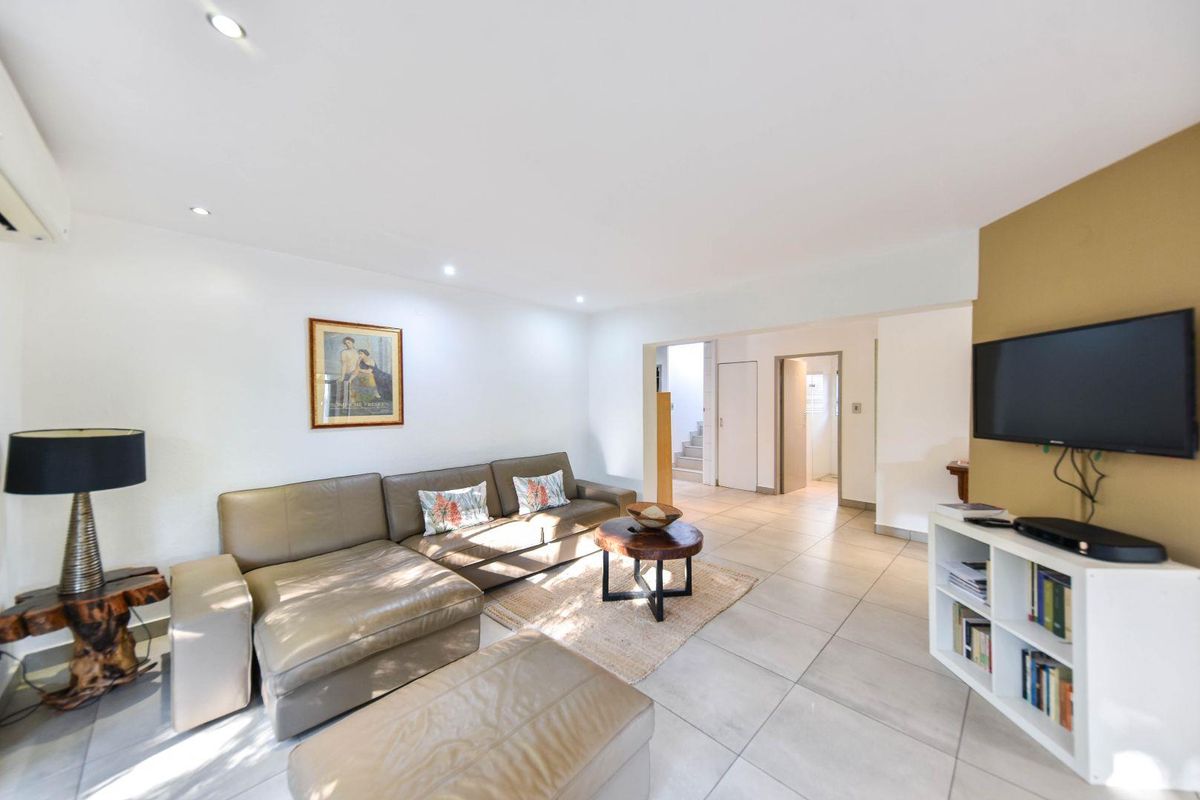 A bright and spacious living room featuring neutral tiled flooring, recessed downlighting, and a wall-mounted air conditioning unit.