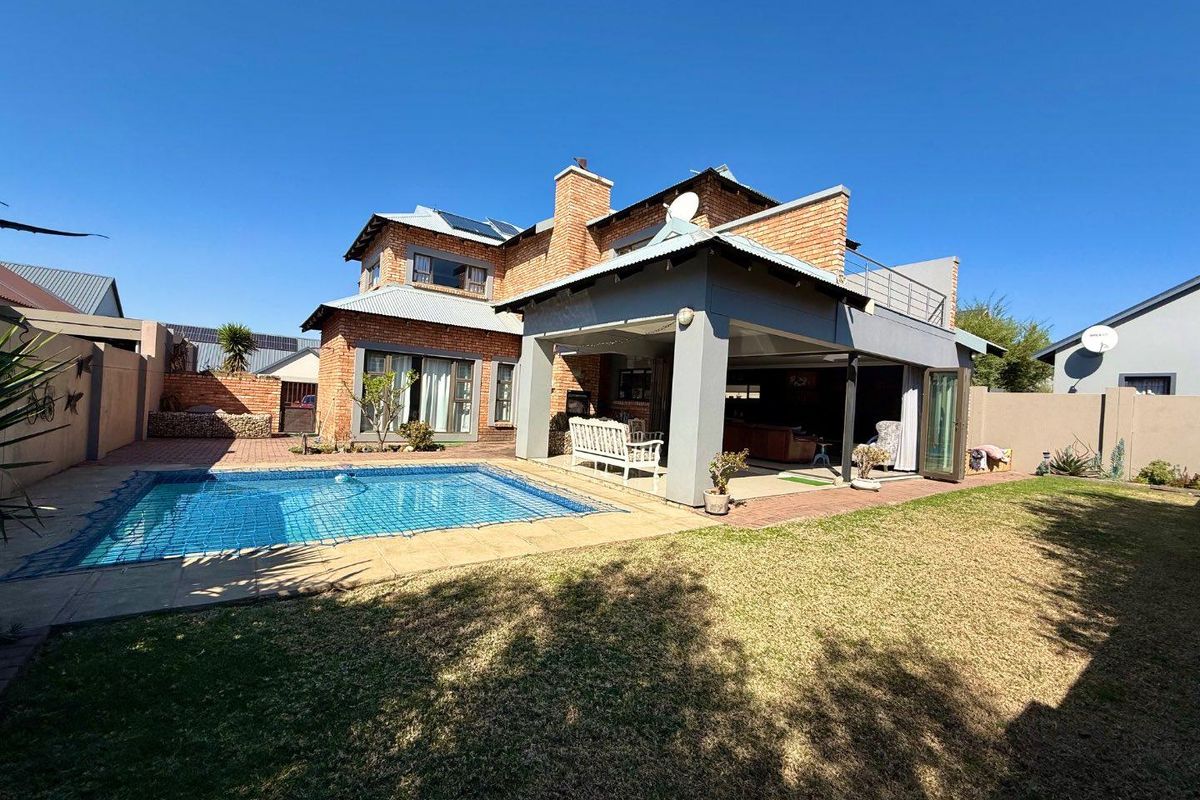 Rear view of a double-story brick house featuring a swimming pool, a covered patio area, and a landscaped garden.