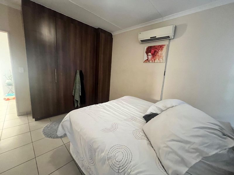 A functional bedroom featuring built-in dark wood cupboards, tiled flooring, and a wall-mounted split-system air conditioning unit.