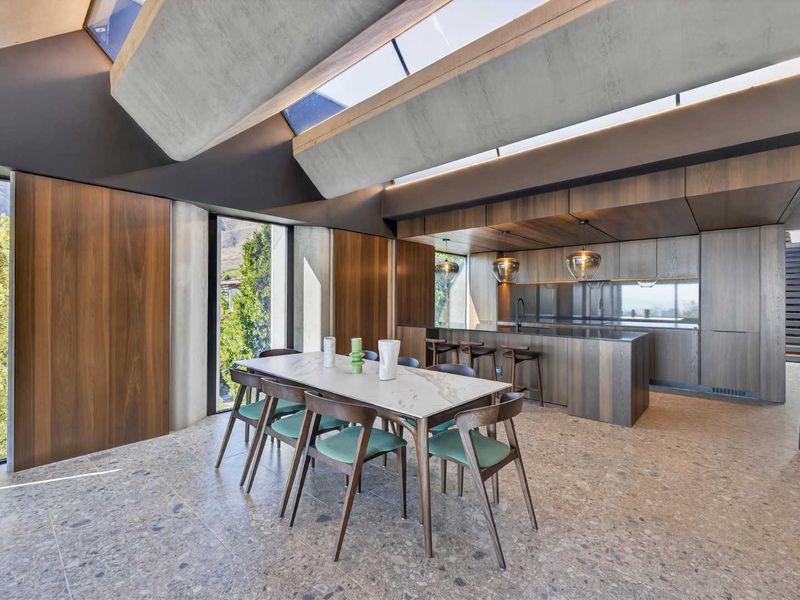 Modern open-plan living and kitchen area featuring high-end timber cabinetry, terrazzo flooring, and striking exposed concrete ceiling beams with integrated skylights.