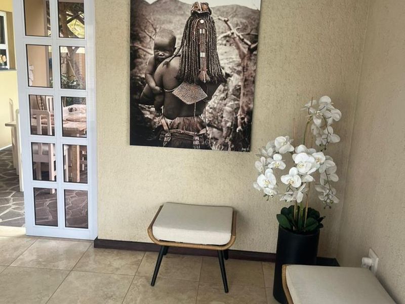 A covered patio area featuring neutral tiled flooring, textured walls, and a white multi-pane glass door leading into the home.