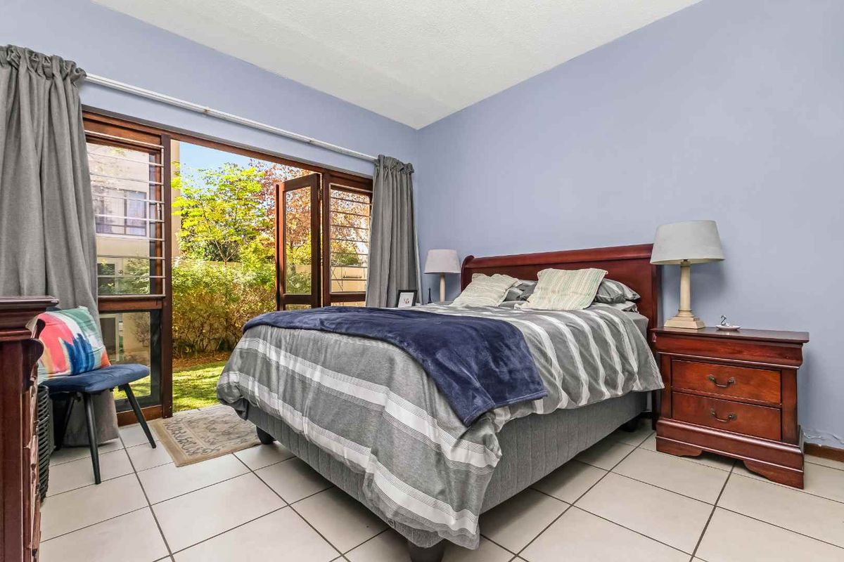A bedroom featuring tiled flooring and large wooden-framed glass doors providing direct access to the garden area.