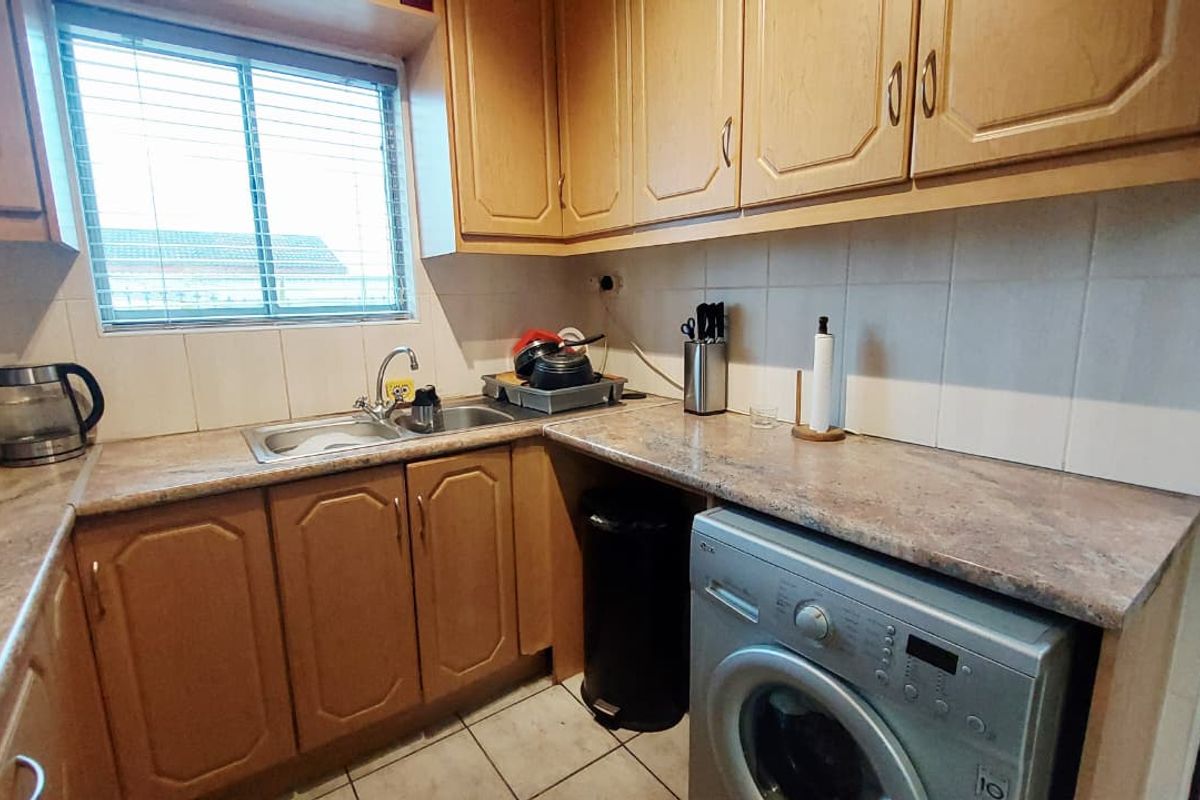 A functional kitchen area featuring laminate countertops, wooden cabinetry, a stainless steel sink, and space for a front-loading washing machine.