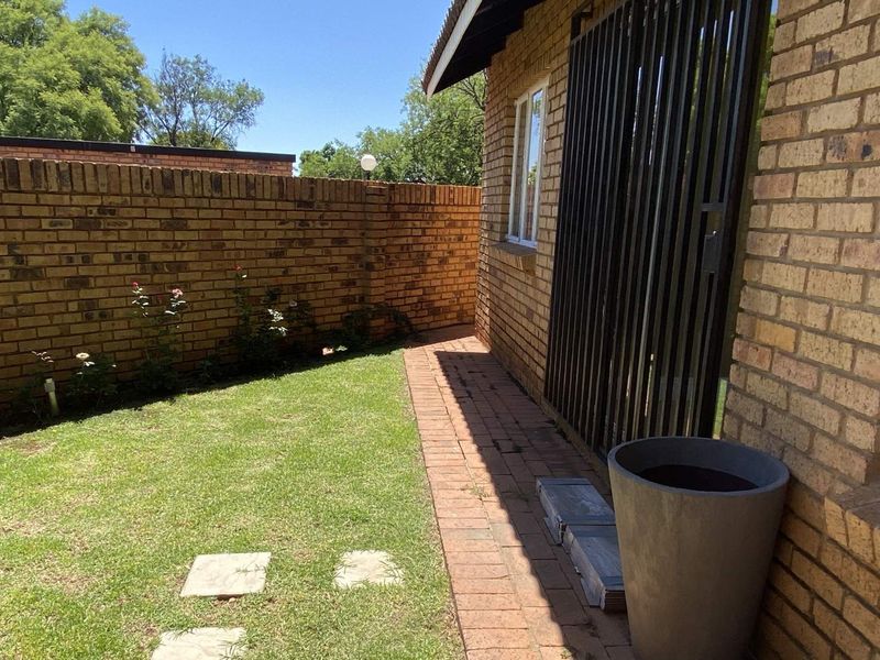 A private rear garden area featuring a well-maintained lawn, paved walkway, and face brick boundary walls, providing a secure outdoor space.