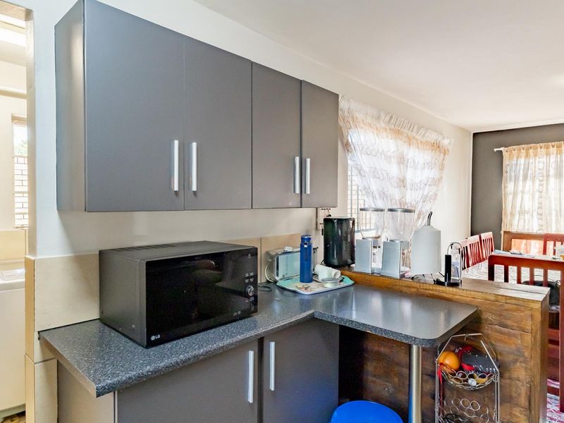 Open plan kitchen area featuring modern grey cabinetry, laminate countertops, and a breakfast bar, seamlessly connecting to the adjacent dining space.