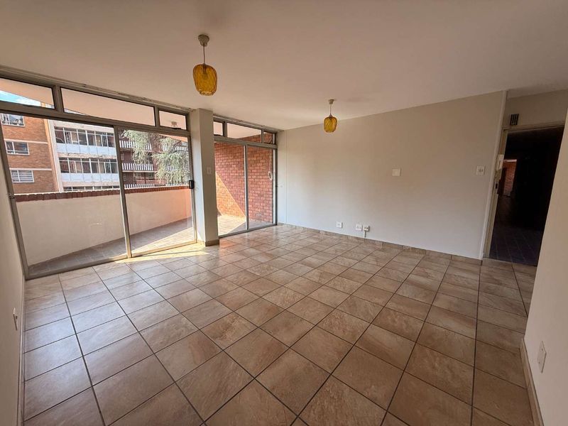 Spacious, empty living area featuring neutral tiled flooring, large sliding glass doors providing natural light, and access to an outdoor balcony.