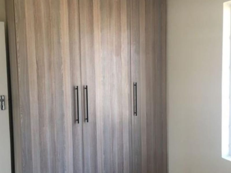 A clean bedroom featuring modern wood-finish built-in cupboards, neutral wall paint, and tiled flooring.