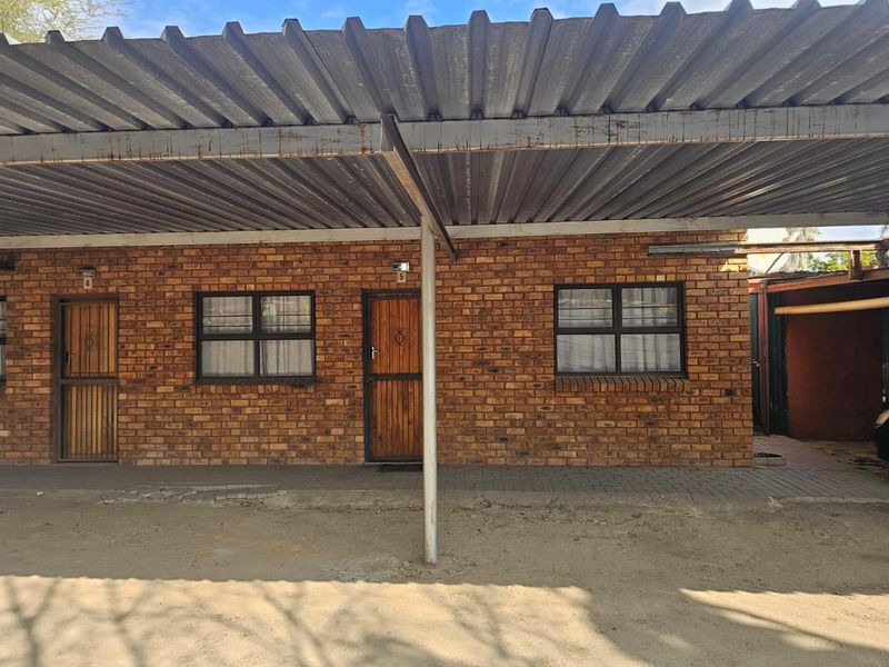 Exterior view of a facebrick residential unit featuring a corrugated metal carport and secure entrance doors.