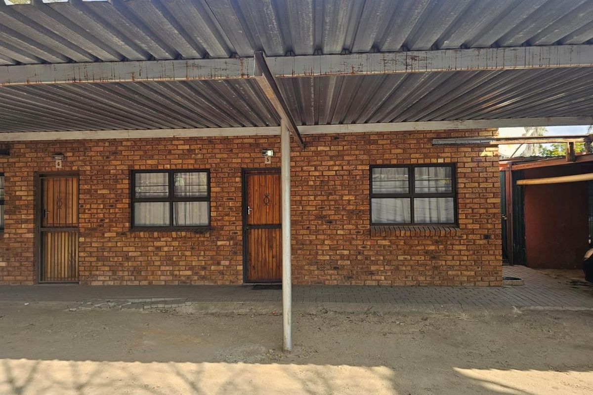Exterior view of a facebrick residential unit featuring a corrugated metal carport and secure entrance doors.