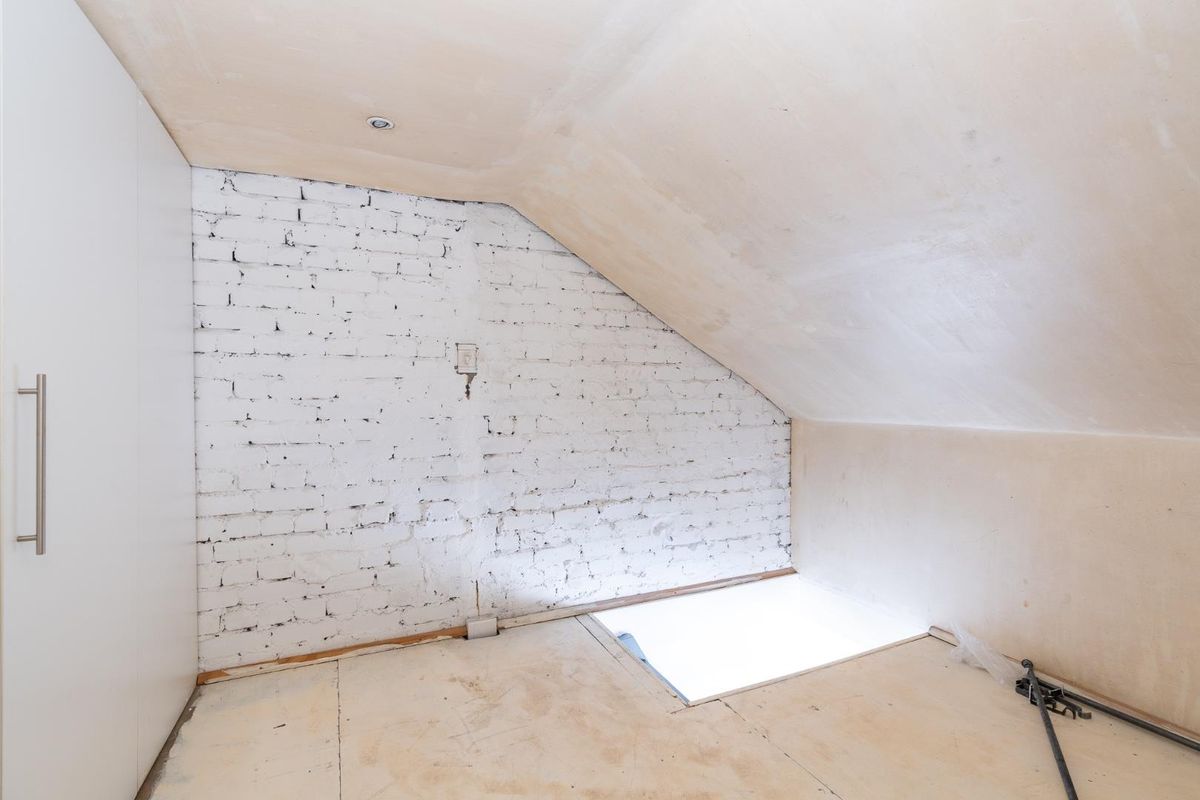 An attic-style bedroom space featuring a painted brick feature wall, built-in wardrobe, and unfinished flooring and ceiling surfaces awaiting final renovation.