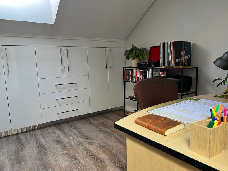 A functional home office featuring custom built-in cabinetry, wood-look laminate flooring, and a skylight providing natural light.