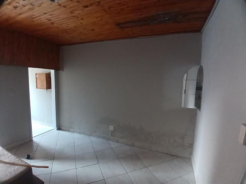 An empty living area featuring ceramic floor tiles and a timber ceiling, showing signs of moisture damage on the lower walls.