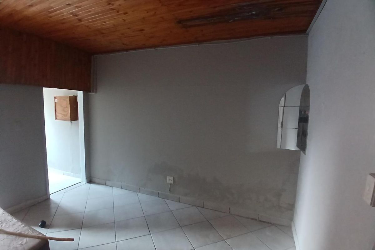 An empty living area featuring ceramic floor tiles and a timber ceiling, showing signs of moisture damage on the lower walls.