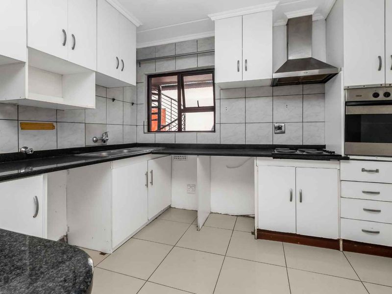 A functional kitchen featuring white cabinetry, granite countertops, a built-in oven, and a stainless steel extractor fan, with tiled flooring and backsplash.