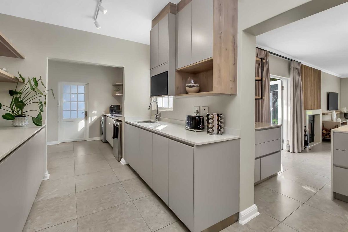 Modern kitchen featuring sleek cabinetry, stone countertops, and integrated appliances, seamlessly flowing into the adjacent living area with tiled flooring throughout.