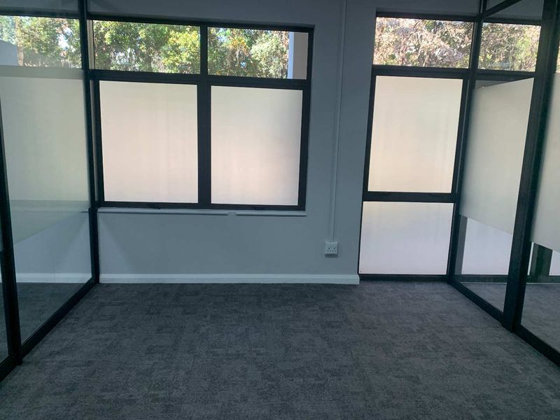 A modern, empty office space featuring glass partitioning, grey carpet flooring, and large windows with frosted privacy film.