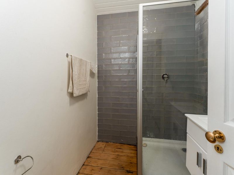 A compact bathroom featuring a shower enclosure with grey subway tiles, a vanity cabinet, and timber flooring, currently requiring finishing touches.