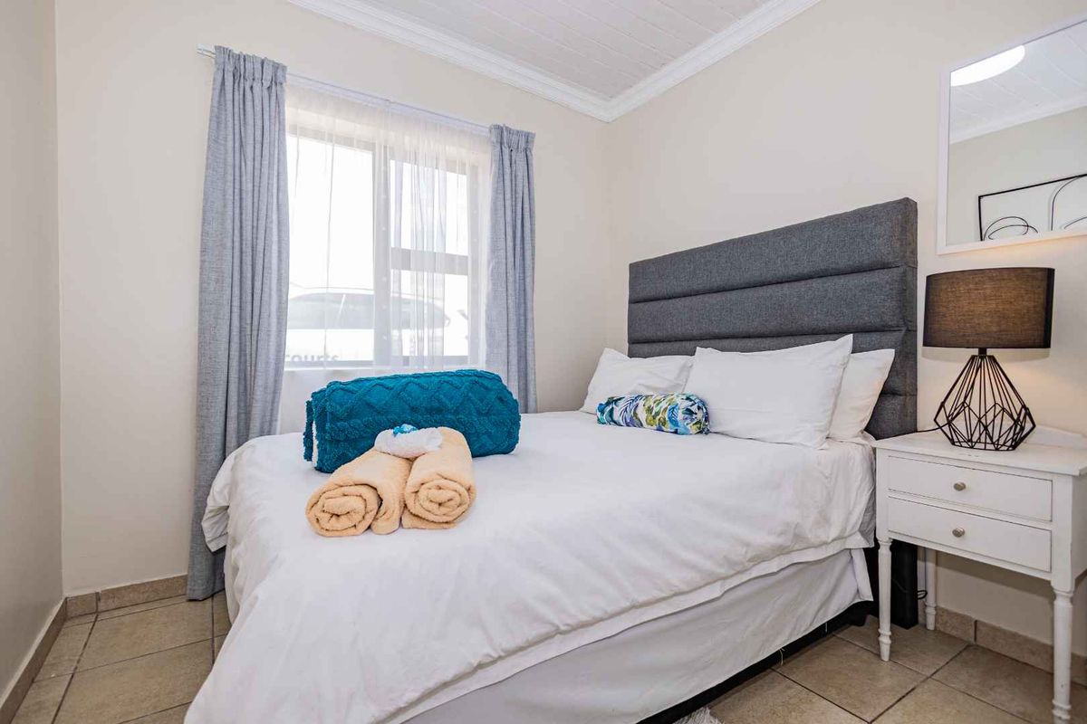 A compact bedroom featuring tiled flooring, a white tongue-and-groove ceiling, and a window with curtain tracks.