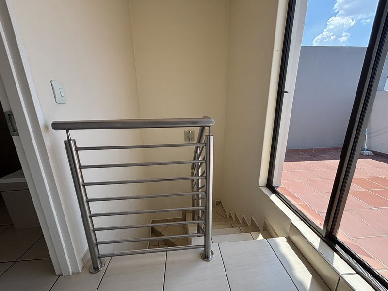 A bright hallway featuring a modern stainless steel balustrade, tiled staircase, and direct access to an outdoor tiled patio through a sliding glass door.