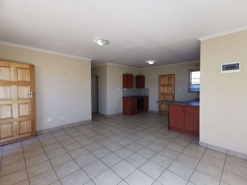An open-plan living and kitchen area featuring tiled flooring, built-in cabinetry, a breakfast counter, and wooden doors.
